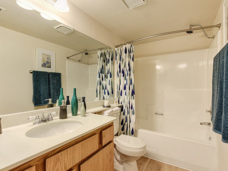 Bathroom with sink vanity and tub/shower combination.  There are accent colors of blue and teal with the bath towels and shower curtains.